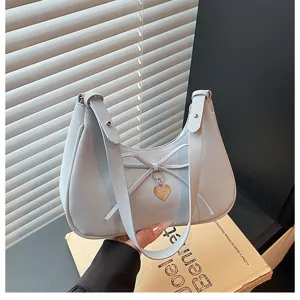 Gros plan détail du sac porté épaule gris clair avec un joli nœud et un pendentif cœur.
