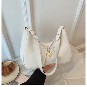 Détail de sac porté épaule blanc avec nœud, pendentif cœur et design élégant.