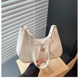 Détail de sac à épaule en cuir blanc, nœud élégant et pendentif en forme de cœur.