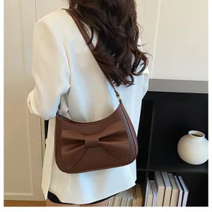 Detail view of stylish brown shoulder bag featuring a chic front bow and elegant leather finish.