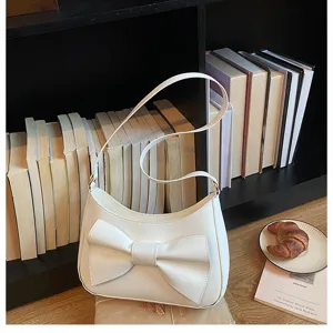 Detailed shot of white shoulder underarm bag with large bow decor in library cafe scene.