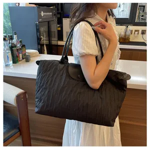 Detail view of the black pleated shoulder bag worn by a model in a casual indoor setting.