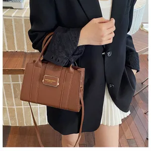 Détail de sac cabas en cuir PU marron avec texture, badge en métal et bandoulière.