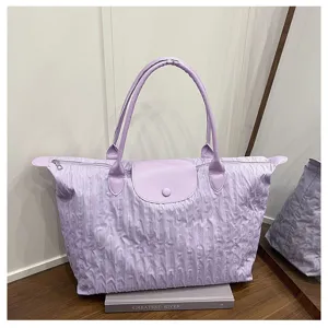 Detail shot of a light purple pleated tote bag with top handle and flap closure on wooden desk.