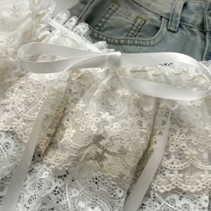 Close-up detail of white layered lace skirt extension with elegant satin ribbon bow ornament.