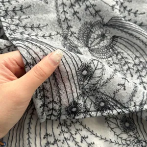 Close-up detail of sheer fabric with elegant black floral vine embroidery, lightweight texture.