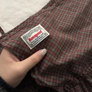 Plaid fabric detail close-up showcasing the brand woven tag, texture and stylish design.