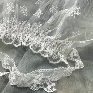 Close-up detail shot of white sheer lace fabric with delicate ruffles and floral embroidery patterns.