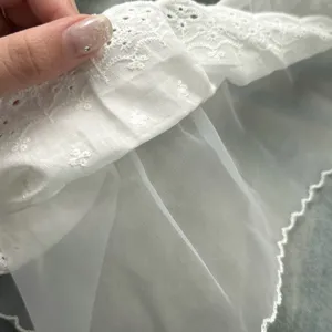 Detailopname van de witte katoenen kantrand en mesh-stof met zeer fijn borduurwerk.
