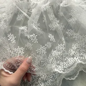 Close-up of exquisite white lace fabric featuring delicate floral embroidery and scalloped edge.