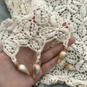 Primo piano dei dettagli del tessuto in pizzo crochet beige con frange di perle di conchiglia.
