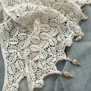 Dettaglio gonna a portafoglio con frange in pizzo uncinetto, maglia beige con conchiglia.