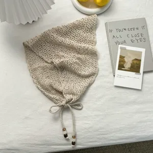Primer plano de pañuelo triangular de punto calado beige con cordón y borlas de cuentas.