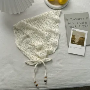 Detalle de pañuelo triangular de punto calado blanco, diseño con borlas y tela suave transpirable.