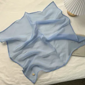 Lichtblauwe chiffon vierkante sjaal detailopname, zachte textuur en delicaat metalen label accent.
