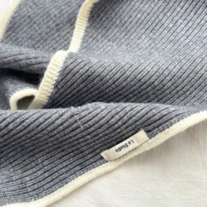 Chal triangular de punto gris con borde blanco contrastante, estilo acogedor y elegante.