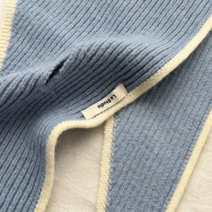 Primer plano detallado de un elegante chal triangular de punto azul con borde blanco y etiqueta.