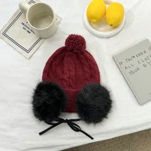 Detailansicht der winterlichen Strickmütze in Weinrot mit flauschigen Ohrenschützern und Schleife.