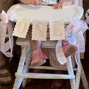Detailed view of pink plaid 1st birthday high chair banner with cute bows for party decor.