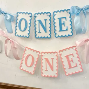 Kids first birthday party banner with blue and pink felt letters and bows for high chair decor.
