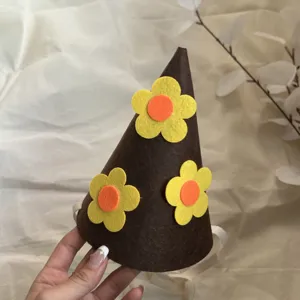 Close-up of brown felt birthday party cone hat with yellow and orange flower detail.