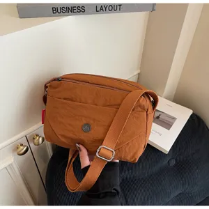 Detail view of a stylish brown nylon crossbody bag with wide strap and metallic logo accent.