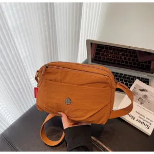 Close-up of casual brown nylon crossbody bag with multi-zip pockets and metal logo.