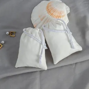 Detailansicht eines weißen Baumwoll-Kordelzugsacks mit Muscheldeko auf grauem Stoff für Schmuck.