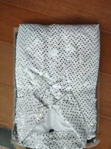 Vista di dettaglio della camicia da uomo con paillettes a pois, piegata nella busta.