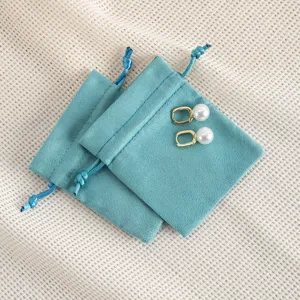 Detailansicht von teal Samt Schmuckbeutel mit Perlenohrringen auf strukturierter Stoff.