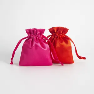 Detailansicht von glänzenden Satin-Kordelzugtaschen in Pink und Rot als Geschenkverpackung.