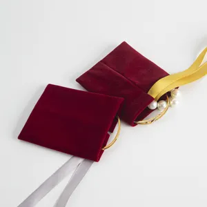 Detailansicht roter Samt-Schmuckbeutel mit dekorativen Armbändern und farbigen Bändern.