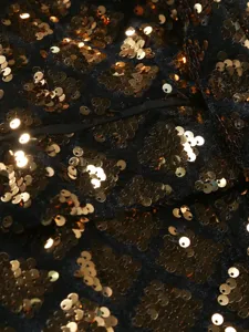 Close-up detail shot of black fabric with sparkling gold sequins, premium garment texture.