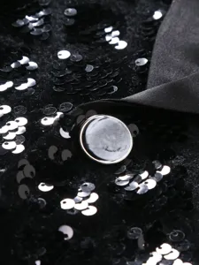 Close-up detail of men's black sequin formal suit fabric, satin lapel and button craftsmanship.