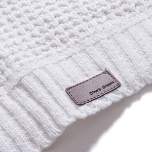 Detail eines weißen Strickpullovers, feines Waffelstruktur-Gewebe mit Lederetikett.