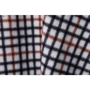 Close-up view of men's trendy knitted sweater fabric with classic black white and brown grid pattern texture