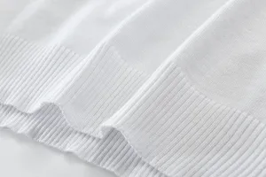 Close-up detail of white knit sweater fabric showing soft ribbed texture and fine craftsmanship.