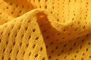 Detailaufnahme von gelbem Strickstoff mit weicher Textur und feinem klassischem Lochmuster.