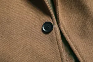 Detail shot of mens thick woolen overcoat fabric and button, classic winter trench coat texture.