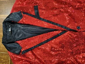 Close-up view of red sequin blazer jacket featuring black satin lapel detail and single button.