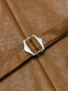 Dettaglio gilet in pelle marrone da uomo con texture fine e fibbia in metallo.