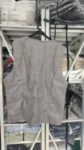 Vue détaillée gilet homme en daim gris, suspendu sur un portant dans un entrepôt.