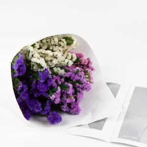 Primo piano dettagliato di un mazzo di fiori secchi colorati avvolti in carta bianca.