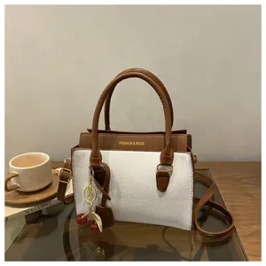 Detail shot of a chic color-block handbag featuring dual top handles and a cute cherry charm.