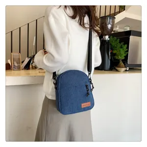 Detail view of blue corduroy crossbody shoulder bag, featuring brown leather logo patch and strap.