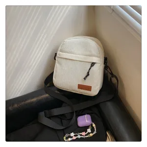 Detailed view of the white corduroy crossbody bag with adjustable strap and front label.