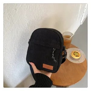 Black corduroy crossbody bag with front zipper pocket and brown brand patch for daily wear.