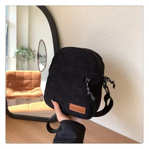 Detailed view of the black corduroy crossbody bag, showing texture, strap and label.