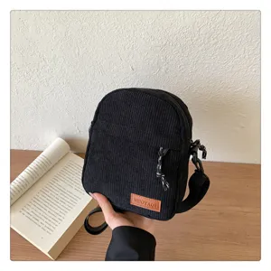Detailed view of black corduroy crossbody bag, showing texture, zipper, and brand tag.