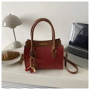Detailed view of color-block handbag with cute cherry charm and dual handles on clean desk.